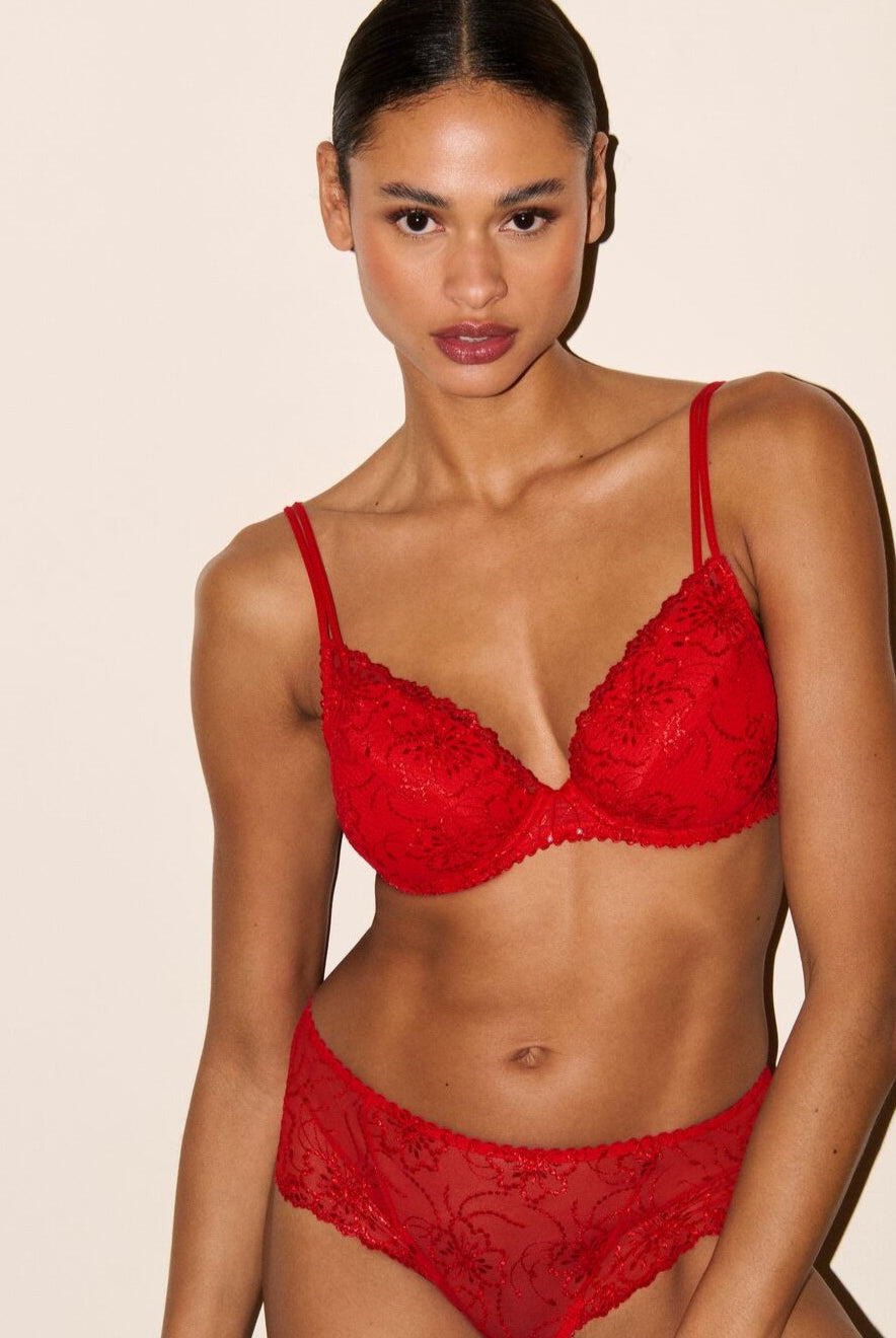 Model wearing a red lace lingerie set against a beige background
