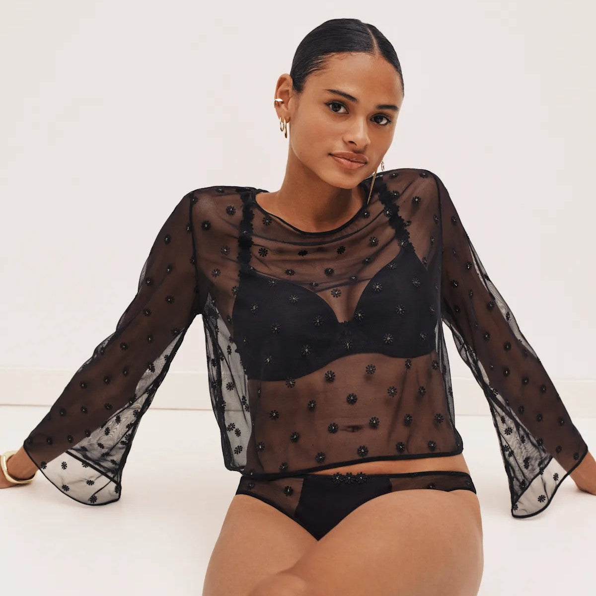 Woman wearing a sheer black long-sleeve top with a white background