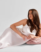 Woman in a white dress lying on a pink blanket against a light gray background