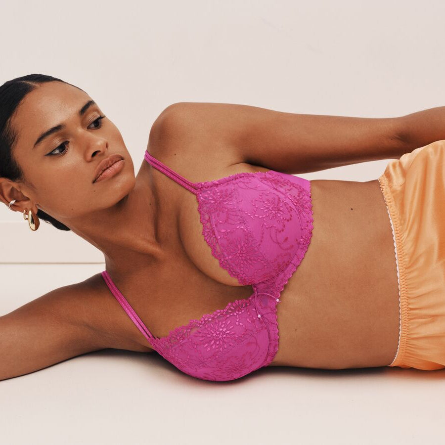 Woman wearing a pink lace bra and orange underwear on a white background