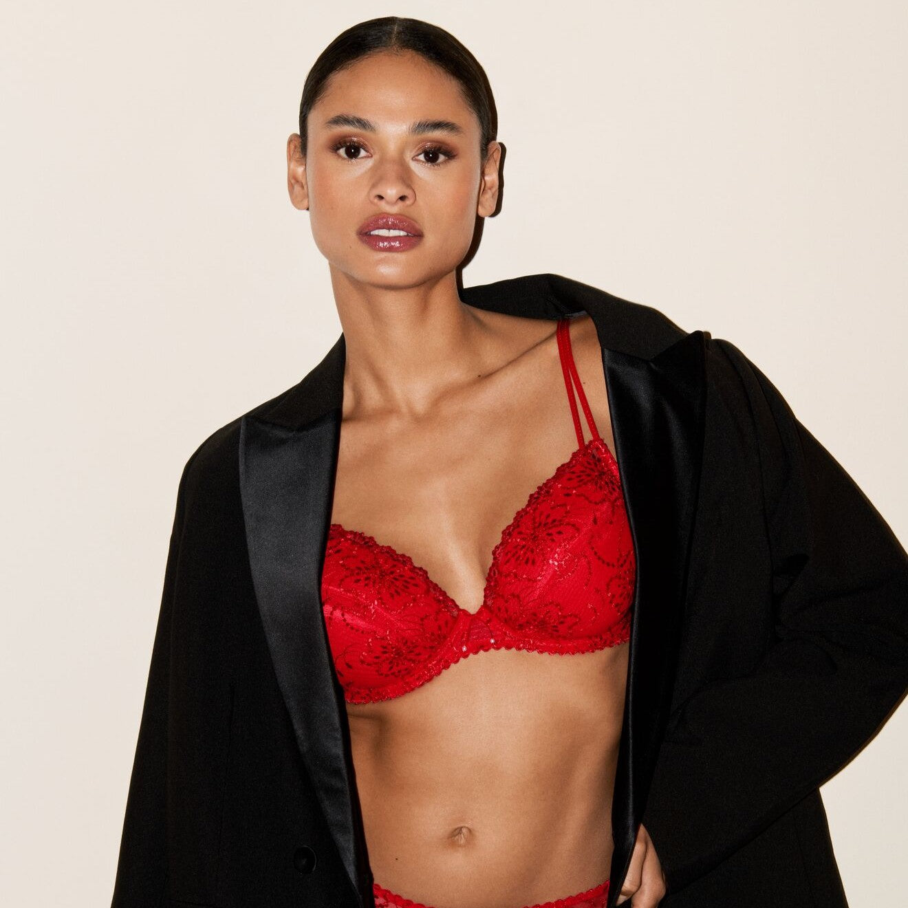 Woman wearing a red bra and black jacket on a beige background