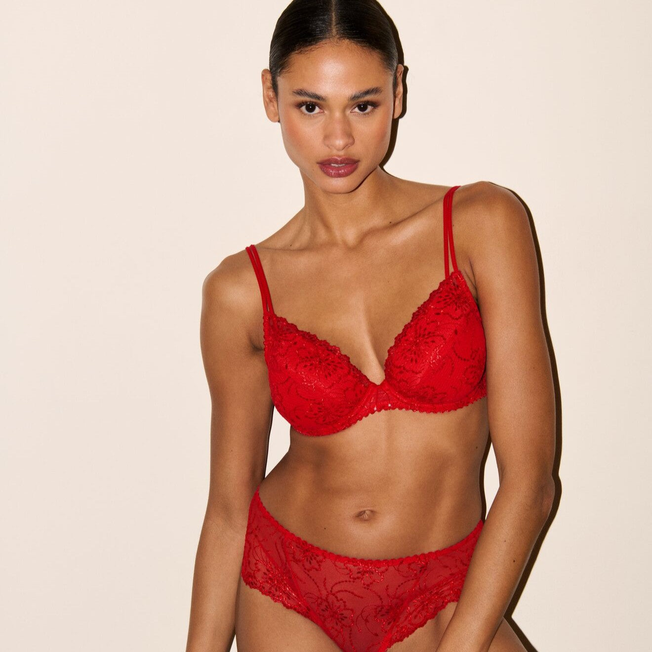 Model wearing a red lace lingerie set against a beige background