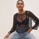 Person wearing a sheer black top with long sleeves and light blue jeans on a white background